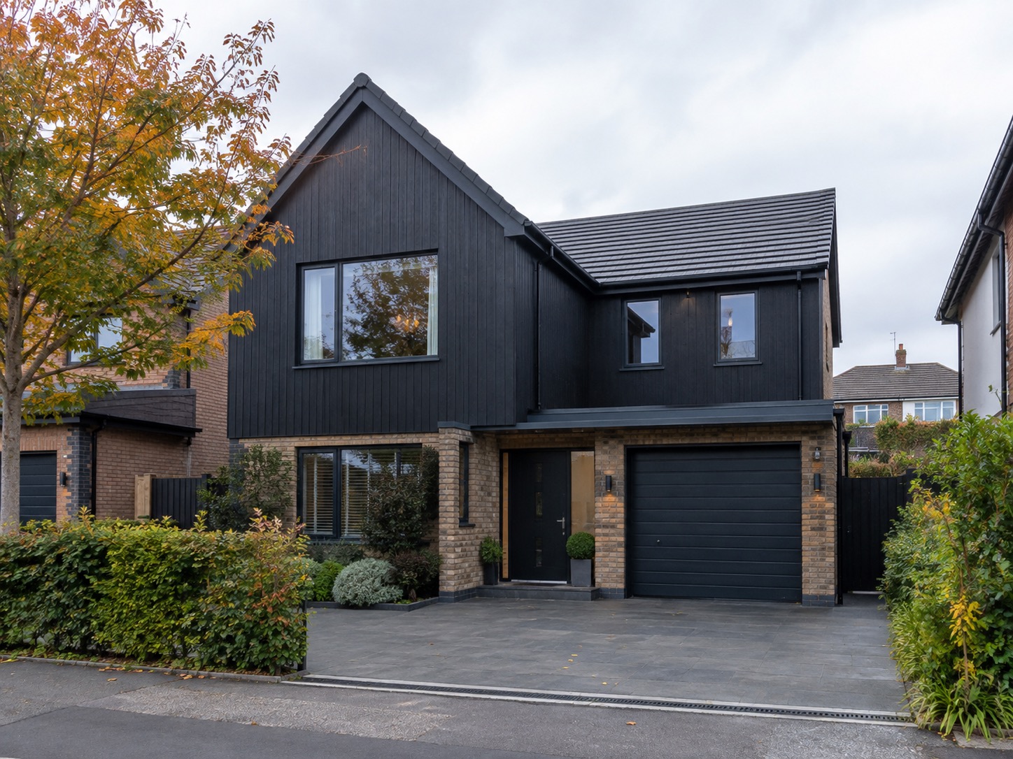Modern detached house with black timber cladding, a brick ground floor, black garage door and a new porcelain-paved driveway